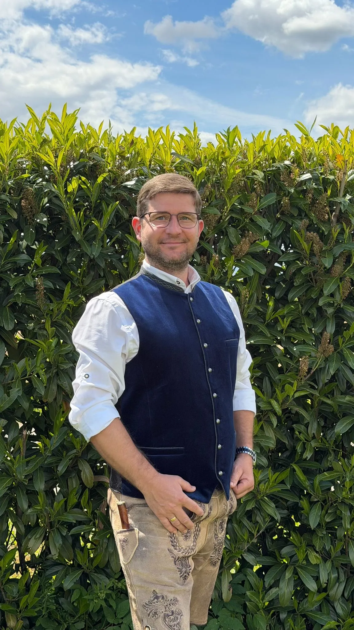 Josef Reiseder im Freien, in blauer Tracht-Weste und Lederhose.